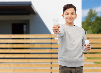 Image showing boy comparing different light bulbs over house