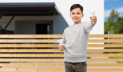 Image showing boy comparing different light bulbs over house