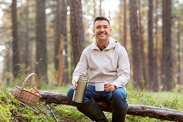 Image showing man with basket of mushrooms drinks tea in forest