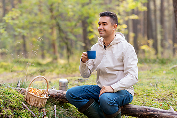 Image showing man with basket of mushrooms drinks tea in forest