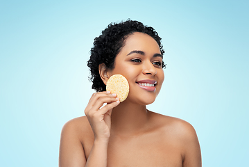 Image showing young woman cleaning face with exfoliating sponge