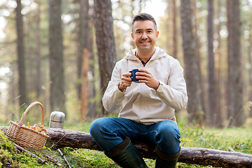 Image showing man with basket of mushrooms drinks tea in forest