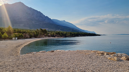 Image showing Beautiful shore of the Adriatic Sea. Sunrise with rays of sun over Biokovo Mountain Nature park and trees from Makarska Riviera-Biokovo, Dalmatia, Croatia, Europe