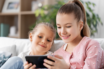 Image showing happy little girls or sisters with phone at home
