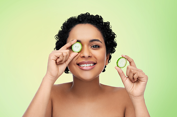 Image showing happy african woman making eye mask of cucumbers