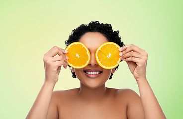 Image showing smiling african woman making eye mask of oranges