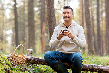 Image showing man with basket of mushrooms drinks tea in forest