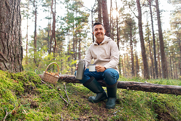 Image showing man with basket of mushrooms drinks tea in forest