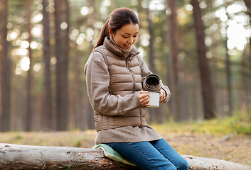 Image showing asian woman with thermos drinking tea in forest