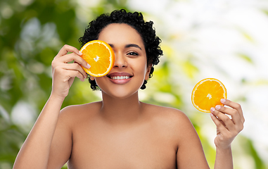 Image showing smiling african woman making eye mask of oranges