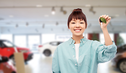 Image showing happy asian woman holding car key with green leaf