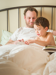 Image showing Chinese and Caucasian Baby Boy Reading a Book In Bed with His Da