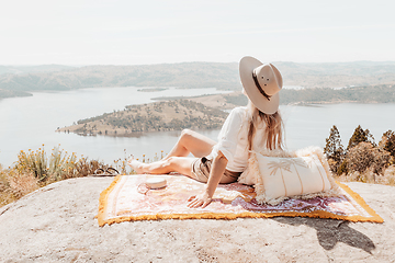 Image showing Woman siting high above water views on woven rug