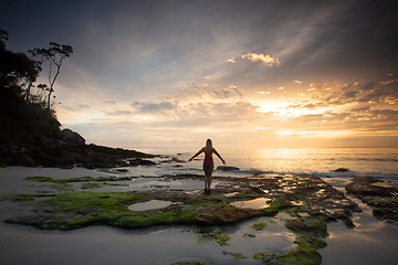 Image showing A woman stands on the beach admiring the sunrise