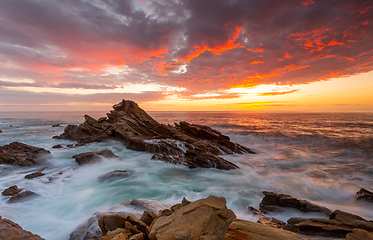 Image showing Sunrise over the ocean and rocky beach foreground