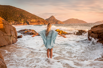 Image showing Woman stands in ocean wabes with a soft pastel sunrise sky