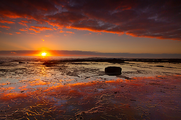 Image showing Seaside sunrise and vivid textured rock reflections