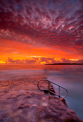 Image showing Rich red stunning sunrise over rock pool and ocean