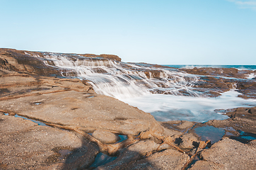 Image showing Milky ocean cascades flowing over honey coloured rocks