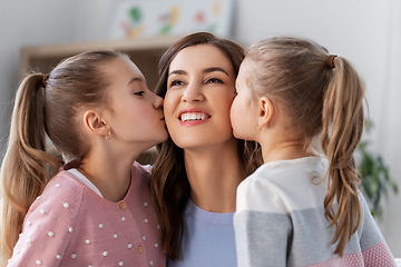 Image showing happy mother and two daughters kissing her at home