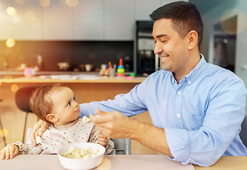 Image showing happy father feeding baby in highchair at home