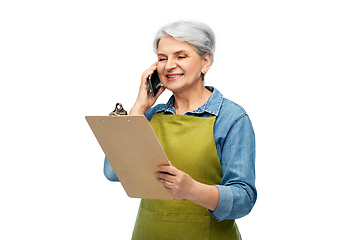 Image showing old female gardener with clipboard calls on phone