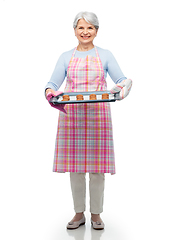 Image showing senior woman in apron with cookies on baking pan