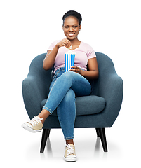 Image showing african woman eating popcorn sitting in armchair