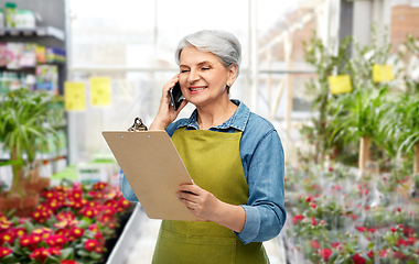 Image showing old female gardener with clipboard calls on phone