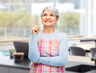 Image showing smiling senior woman in apron pointing finger up