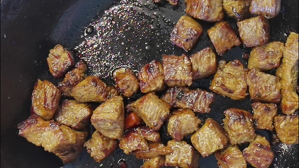 Image showing Pieces of meat are fried in sizzling oil in a hot skillet. Bachelor breakfast, easy to cook food. The cook mixes the meat with a wooden spatula. Macro, close-up view. Frying meat, stove top.