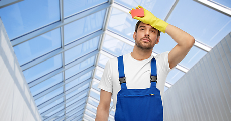 Image showing tired male cleaner with sponge in glasshouse