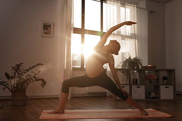 Image showing pregnant woman doing yoga at home over sunshine