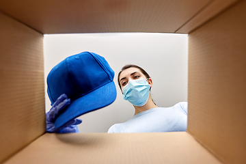 Image showing woman in mask opening parcel box with clothes