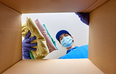 Image showing woman in mask packing clothes to parcel box