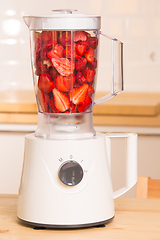 Image showing fresh strawberries in white Blender on a wooden table