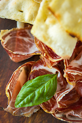 Image showing Homemade prosciutto and basil on a wooden board