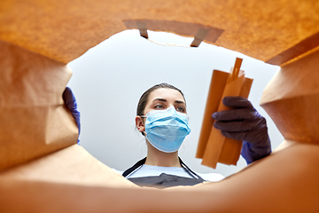 Image showing saleswoman in gloves and mask packing food in bag