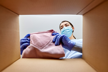 Image showing woman in mask opening parcel box with clothes