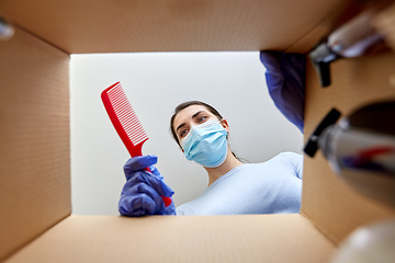 Image showing woman in mask unpacking parcel box with cosmetics