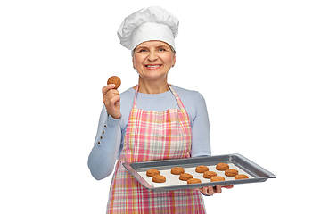 Image showing senior woman in toque with cookies on baking pan