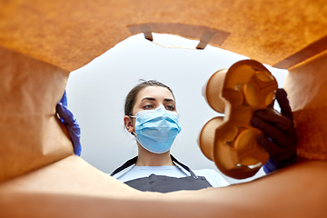 Image showing saleswoman in gloves and mask packing food in bag