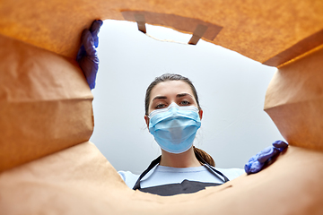 Image showing saleswoman in gloves and mask packing food in bag