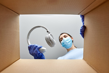 Image showing woman in mask packing headphones into parcel box