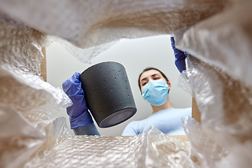 Image showing woman in mask opening parcel box with flower pot