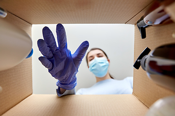 Image showing woman in mask unpacking parcel box with cosmetics