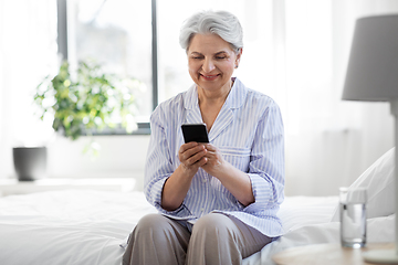 Image showing happy senior woman with smartphone on bed at home