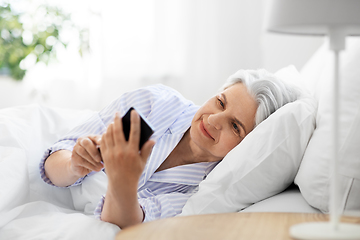 Image showing happy senior woman with smartphone in bed at home