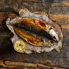 Image showing Fish with lime on parchment paper on a black wooden background. Top view.