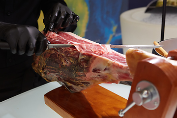 Image showing Sliced dried chamon prosciutto. A man cuts a jamon, a warm toned